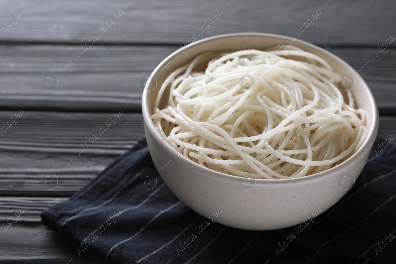 Photo of Bowl of tasty cooked rice noodles and napkin on black wooden table, closeup