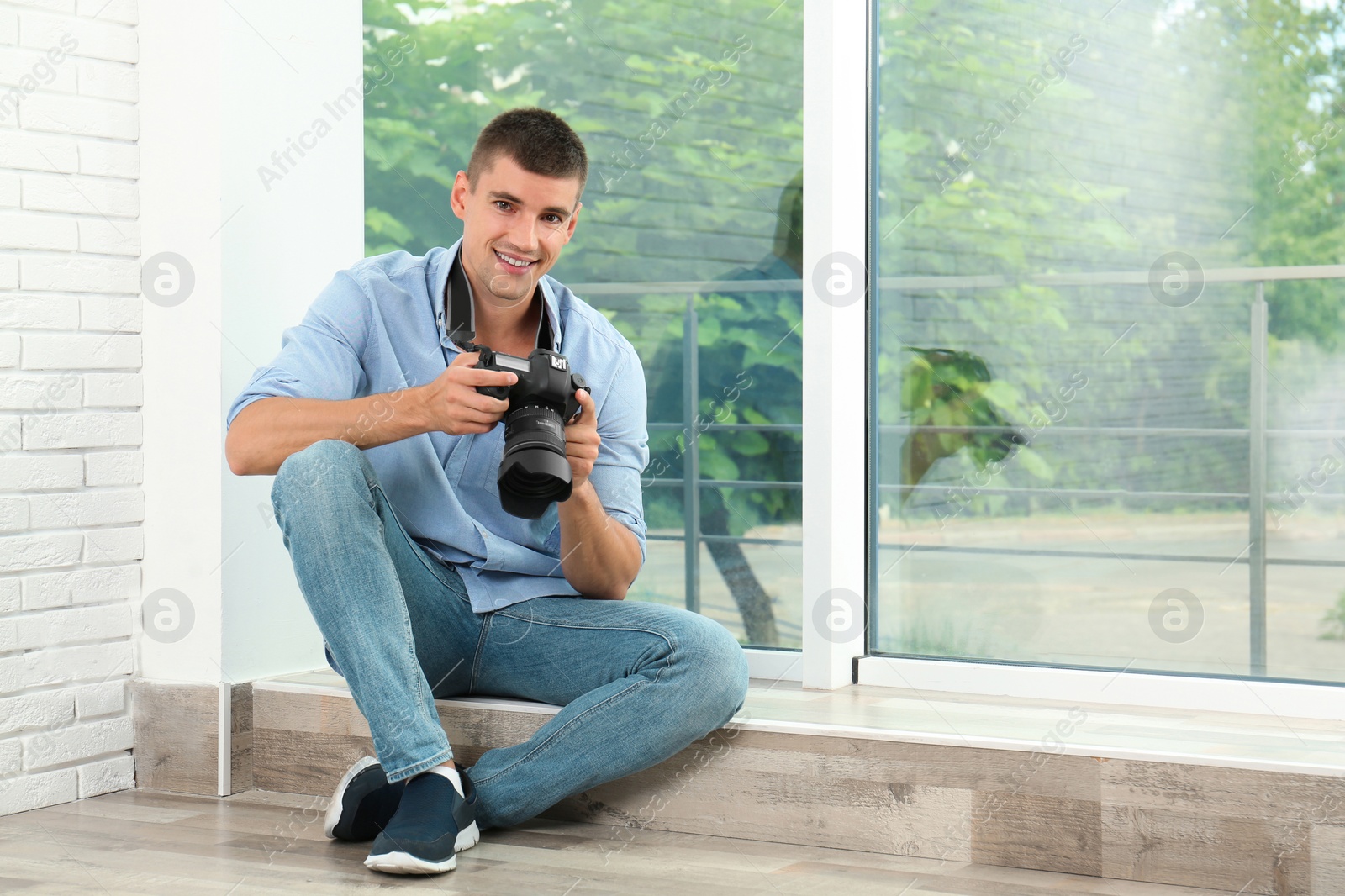 Photo of Young photographer with professional camera near window indoors. Space for text