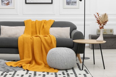 Stylish living room interior with comfortable sofa, blanket, side table and ottoman