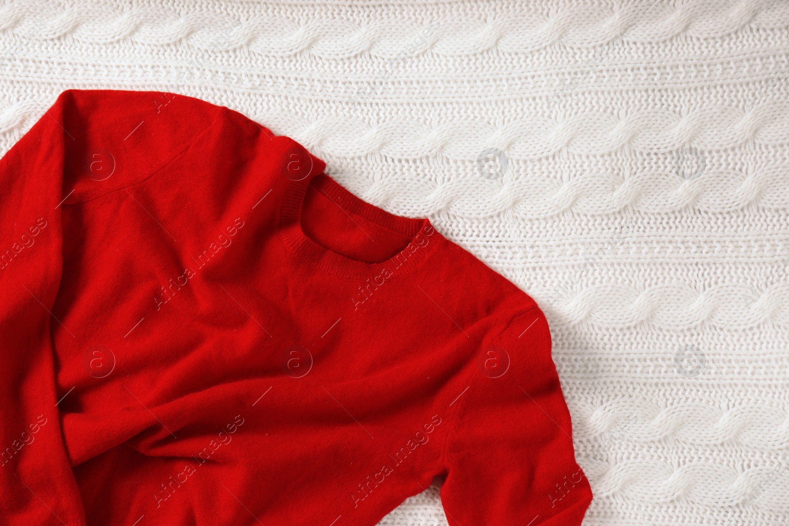 Photo of Red cashmere sweater on white knitted plaid. Space for text