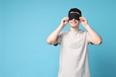 Photo of Happy man in pyjama and sleep mask on light blue background, space for text