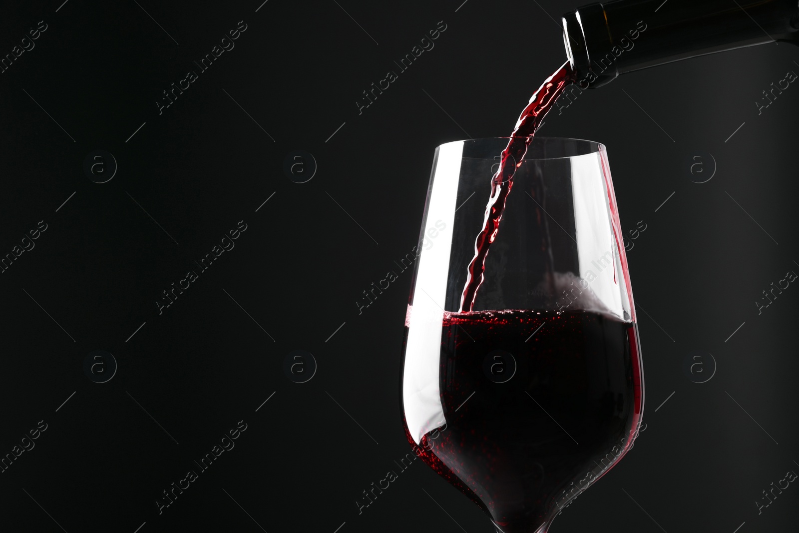 Photo of Pouring red wine into glass against black background, closeup. Space for text