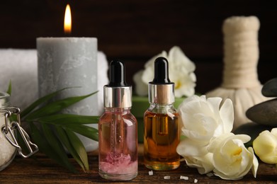 Photo of Bottles with essential oils and flowers on wooden table. Spa products