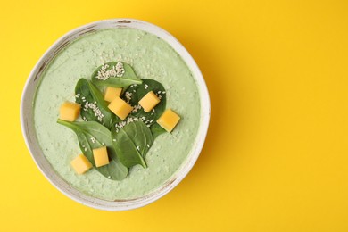 Photo of Delicious spinach cream soup with cheese in bowl on yellow background, top view. Space for text