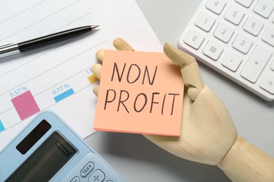 Non Profit concept. Flat lay composition with paper note in wooden mannequin hand on light grey table