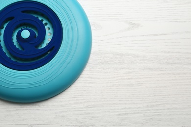 Photo of Blue plastic frisbee disk on white wooden background, top view. Space for text