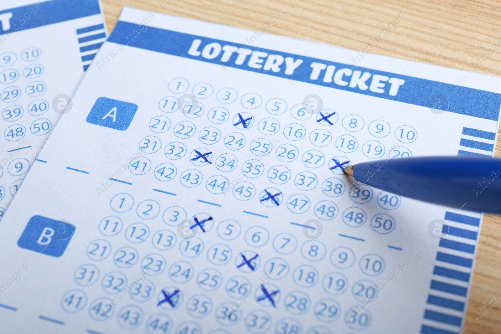 Photo of Filling out lottery tickets with pen on wooden table, closeup. Space for text