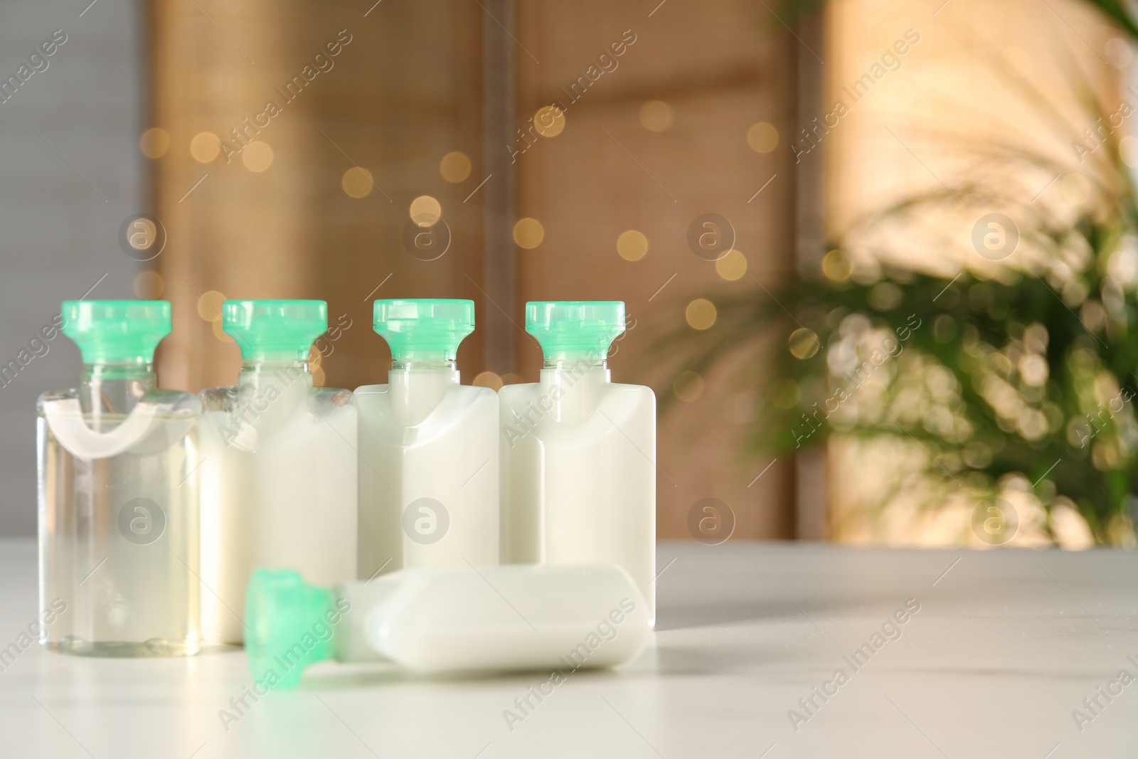 Photo of Mini bottles of cosmetic products on white table against blurred background. Space for text