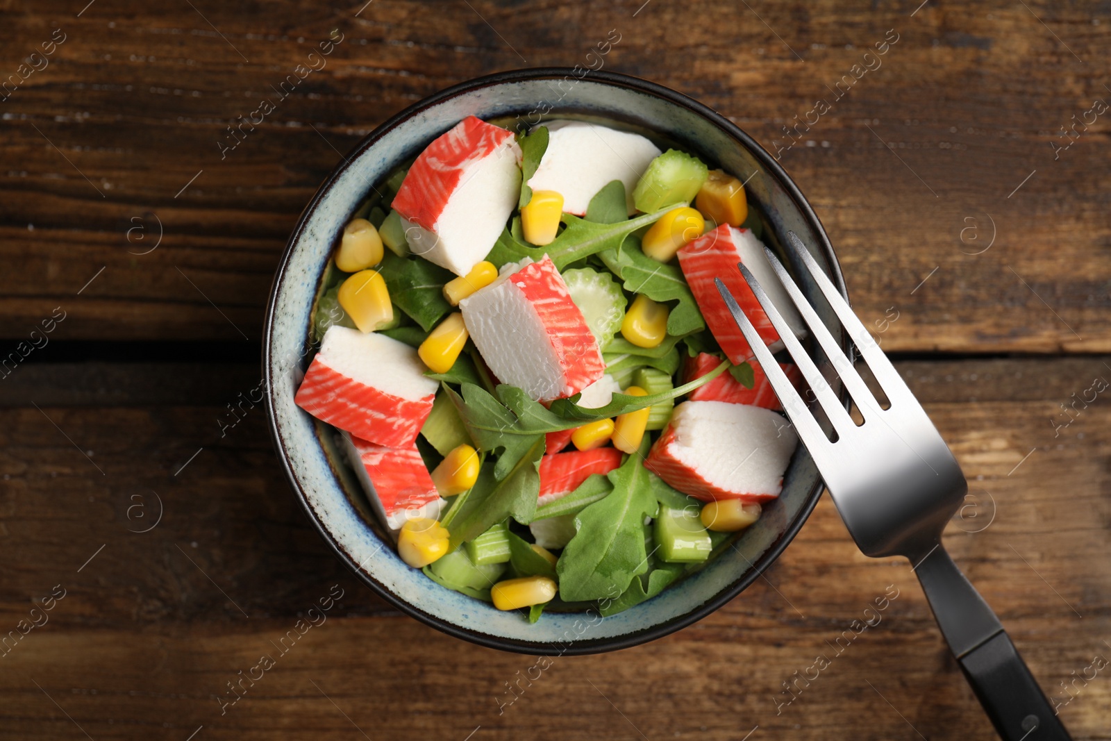 Photo of Tasty crab stick salad and fork on wooden table, top view