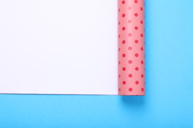 Roll of polka dot wrapping paper on light blue background, top view