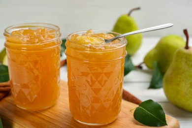 Photo of Delicious pear jam in glass jars on wooden board, closeup