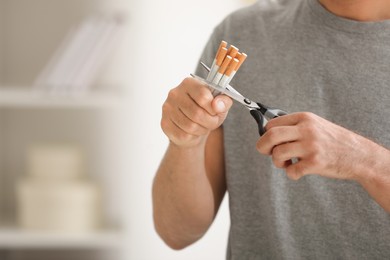 Photo of Stop smoking concept. Man cutting cigarettes on blurred background, closeup. Space for text