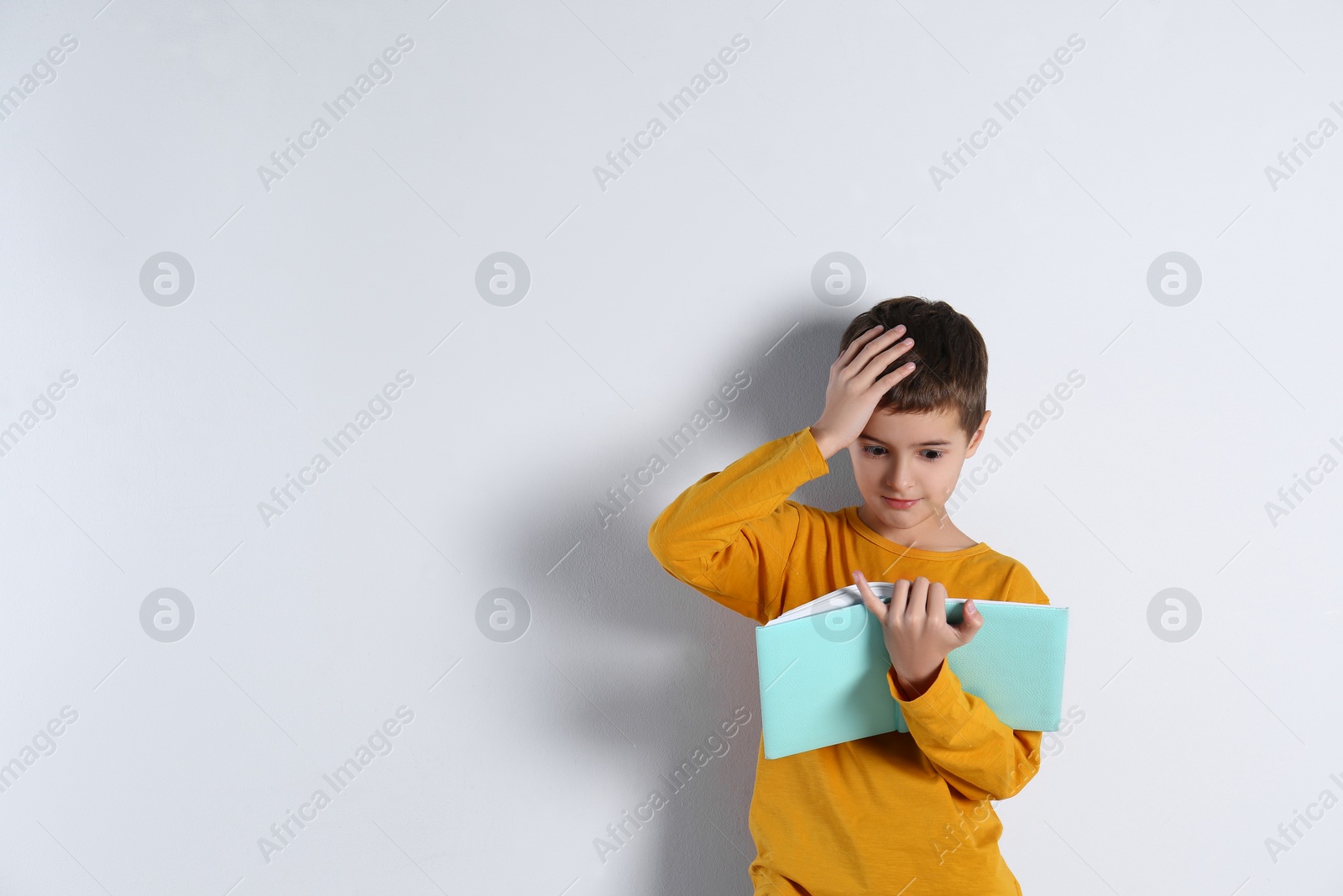 Photo of Cute little boy with book on light background, space for text