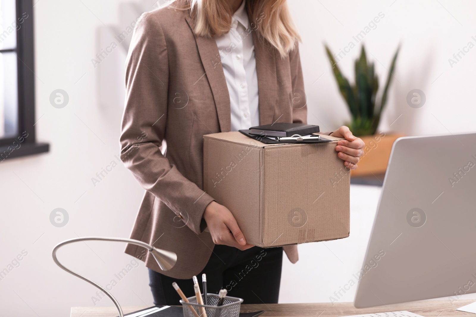 Photo of Young woman holding moving box with office stuff indoors, closeup