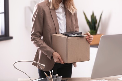 Young woman holding moving box with office stuff indoors, closeup