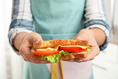 Photo of Woman holding tasty sandwich with cheese and tomato on light background, closeup