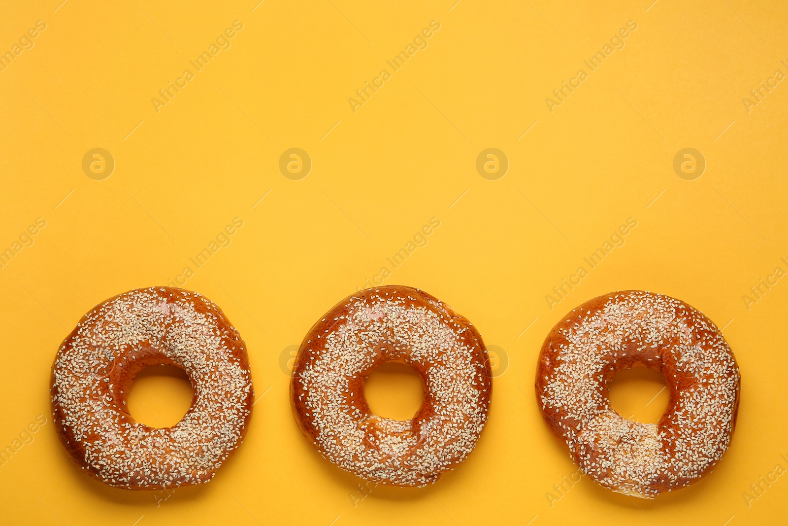 Photo of Delicious fresh bagels with sesame seeds on orange background, flat lay. Space for text