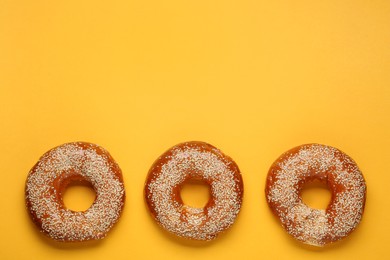 Photo of Delicious fresh bagels with sesame seeds on orange background, flat lay. Space for text