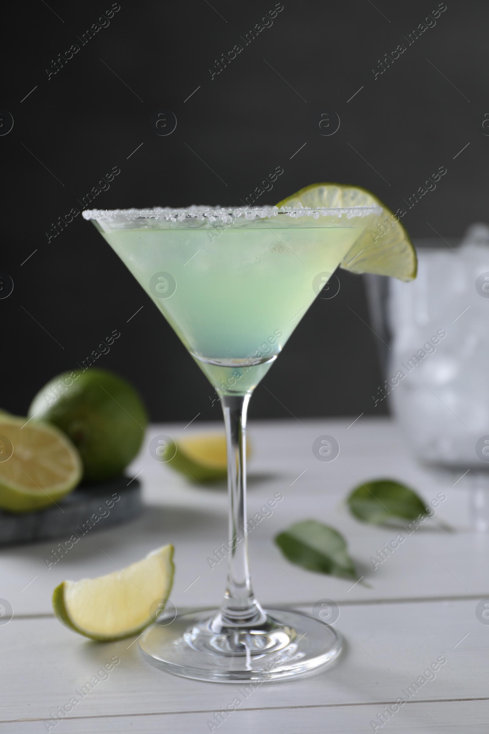 Photo of Delicious Margarita cocktail in glass and limes on white wooden table