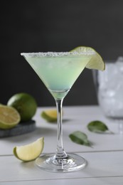 Delicious Margarita cocktail in glass and limes on white wooden table