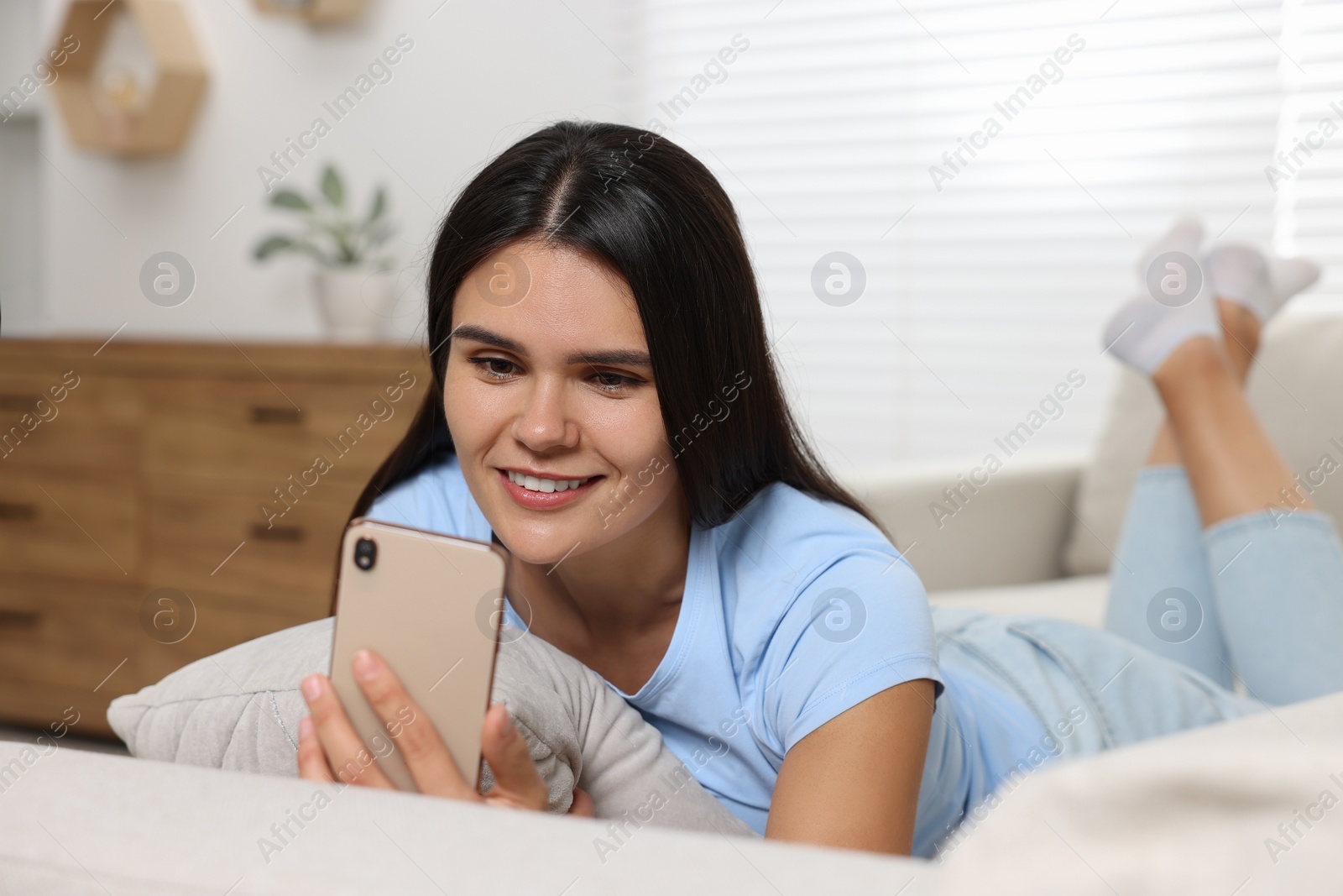 Photo of Happy young woman having video chat via smartphone on sofa in living room