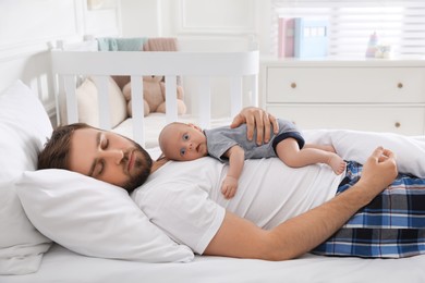 Photo of Tired young father sleeping with his baby in bed at home