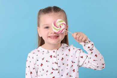 Photo of Happy little girl with colorful lollipop swirl on light blue background
