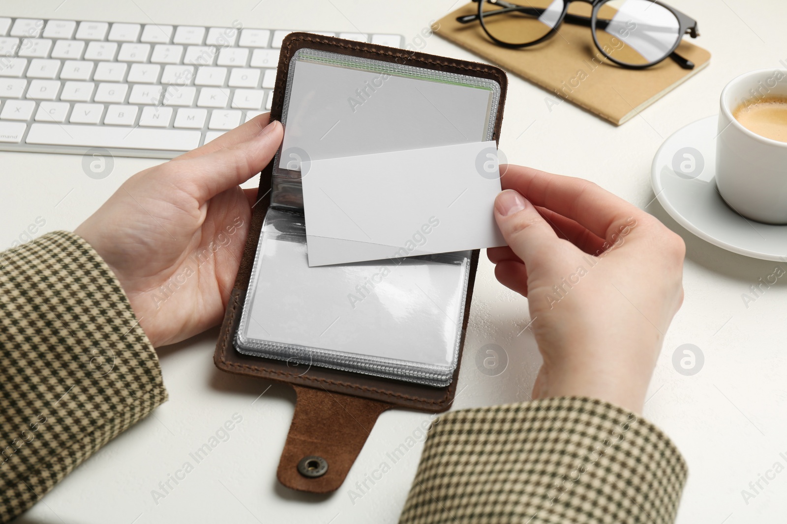 Photo of Woman holding leather business card holder with blank cards at white table, closeup