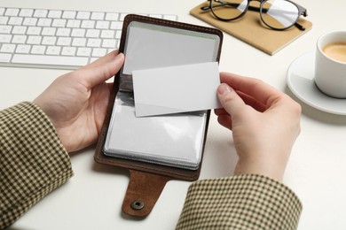 Woman holding leather business card holder with blank cards at white table, closeup