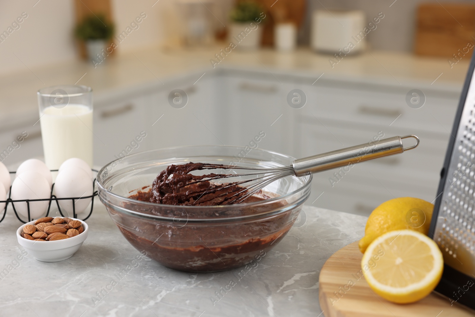 Photo of Metal whisk, chocolate cream in bowl and different products on gray marble table indoors