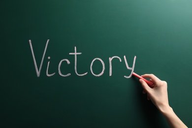 Photo of Young woman writing word Victory on chalkboard