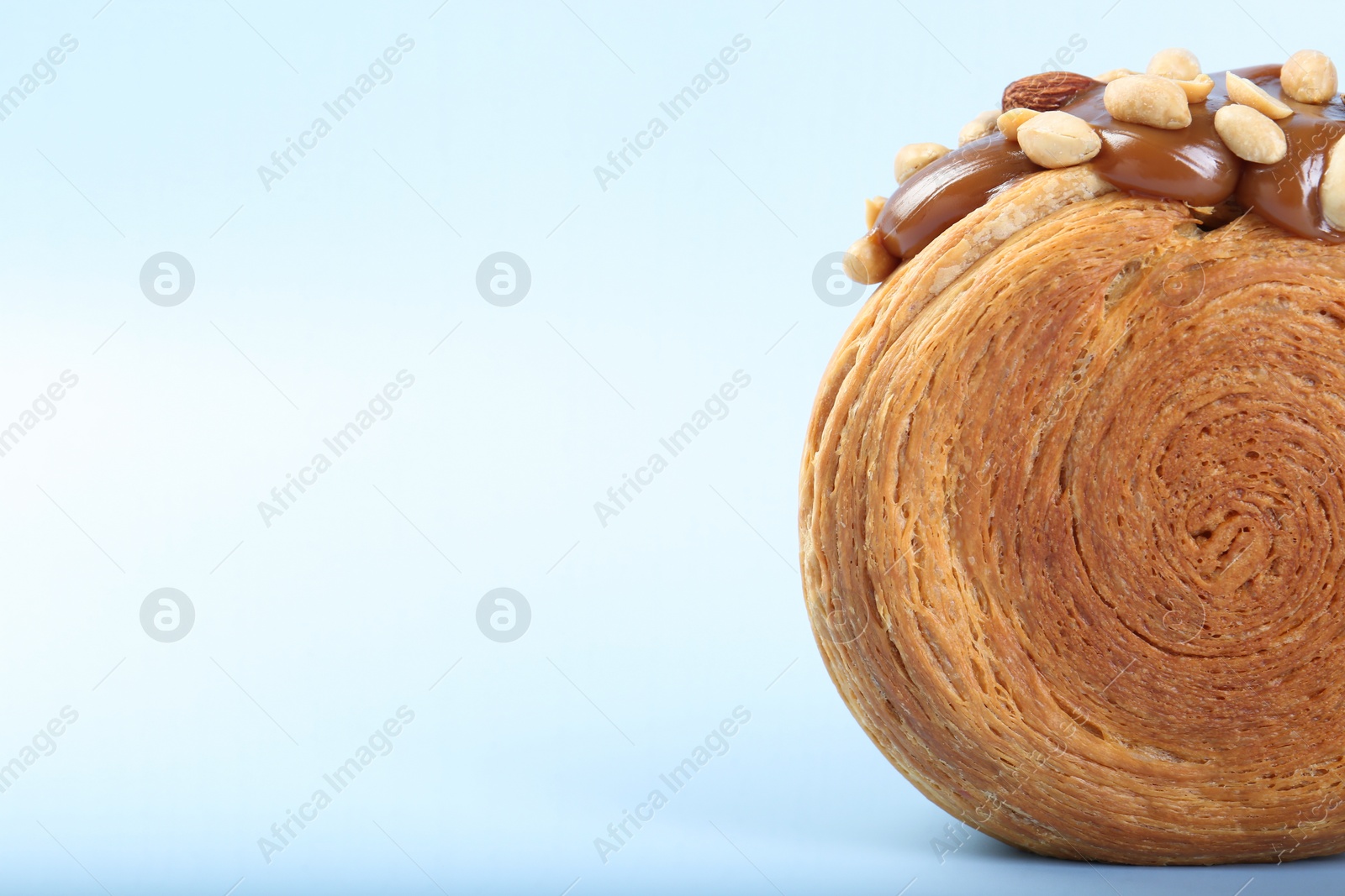 Photo of One supreme croissant with chocolate paste and nuts on light blue background, closeup with space for text. Tasty puff pastry