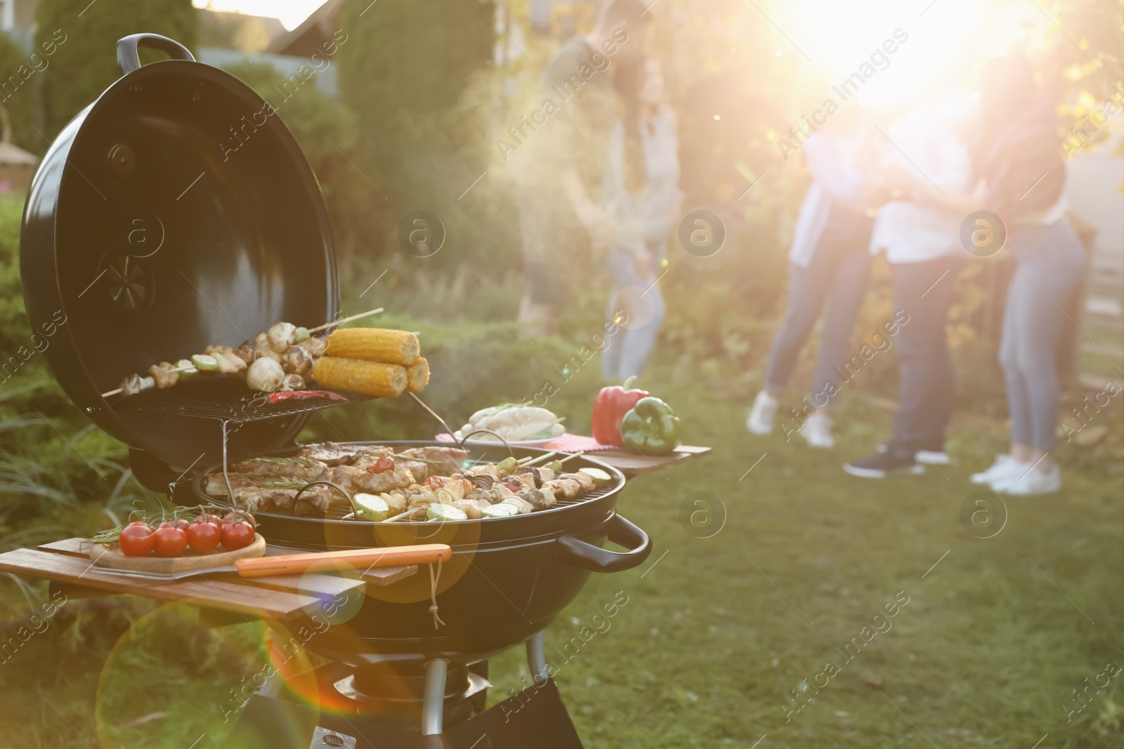 Photo of Group of friends having party outdoors. Focus on barbecue grill with food. Space for text