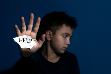 Abused little boy with sign HELP near blue wall, focus on hand. Domestic violence concept