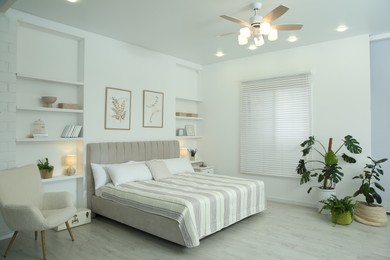 Photo of Comfortable furniture, ceiling fan, houseplants and accessories in stylish bedroom