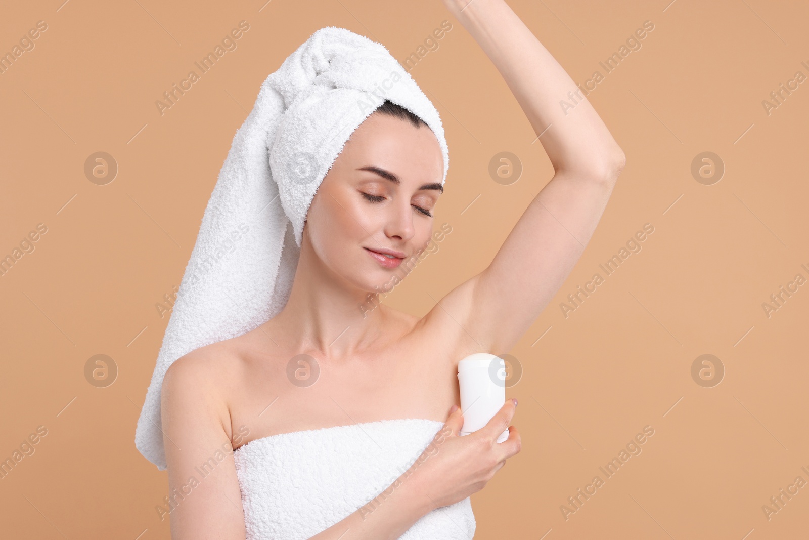 Photo of Beautiful woman applying deodorant on beige background