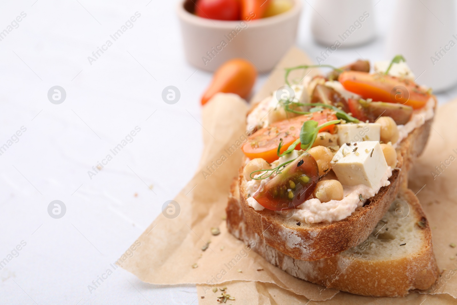 Photo of Tasty vegan sandwich with tomatoes, tofu and chickpeas on white textured table, closeup. Space for text