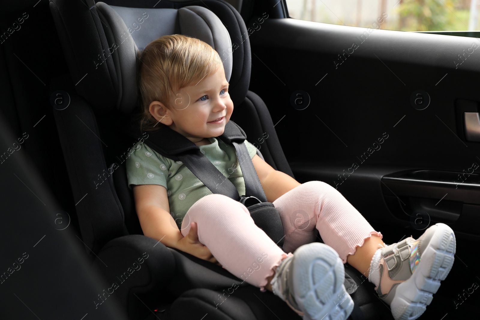 Photo of Cute little girl sitting in child safety seat inside car