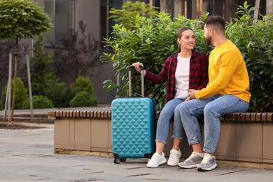 Photo of Long-distance relationship. Beautiful happy couple on bench and suitcase outdoors