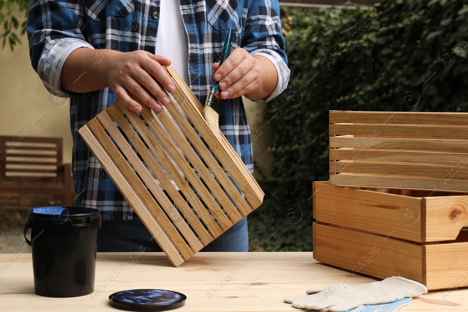 Photo of Man applying varnish onto wooden crate at table outdoors, closeup