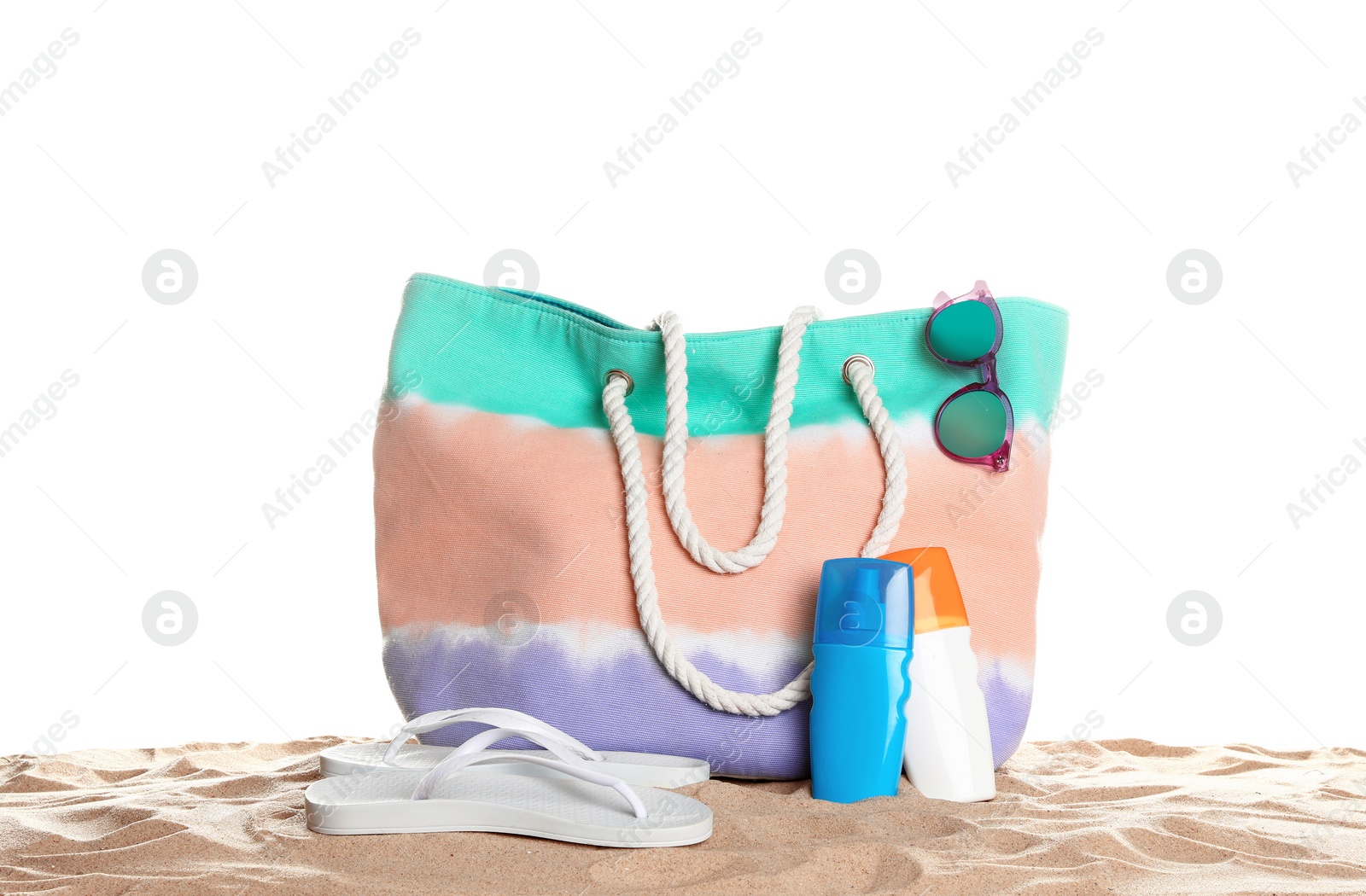 Photo of Stylish colorful bag and beach accessories on sand against white background