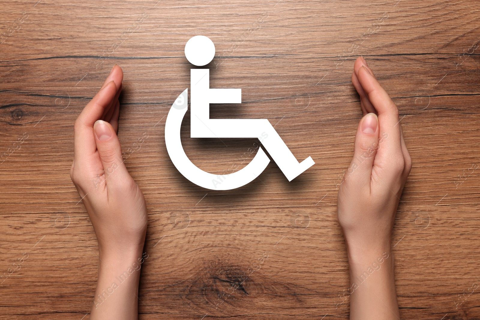 Image of Disability inclusion. Woman protecting wheelchair symbol on wooden background, closeup