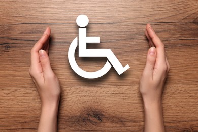 Image of Disability inclusion. Woman protecting wheelchair symbol on wooden background, closeup