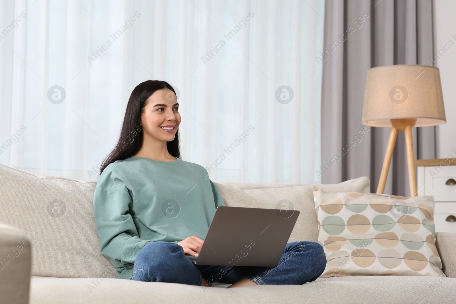 Photo of Happy woman working with laptop on sofa at home