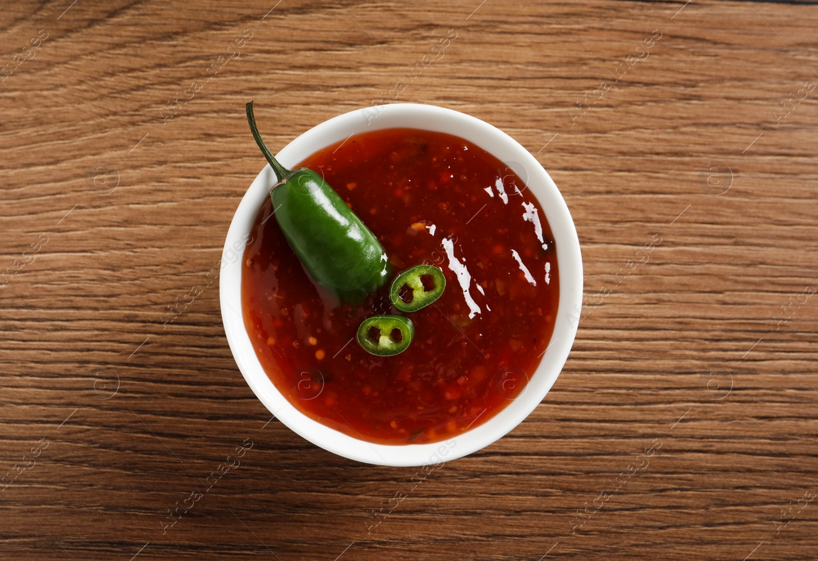 Photo of Spicy chili sauce in bowl on wooden table, top view