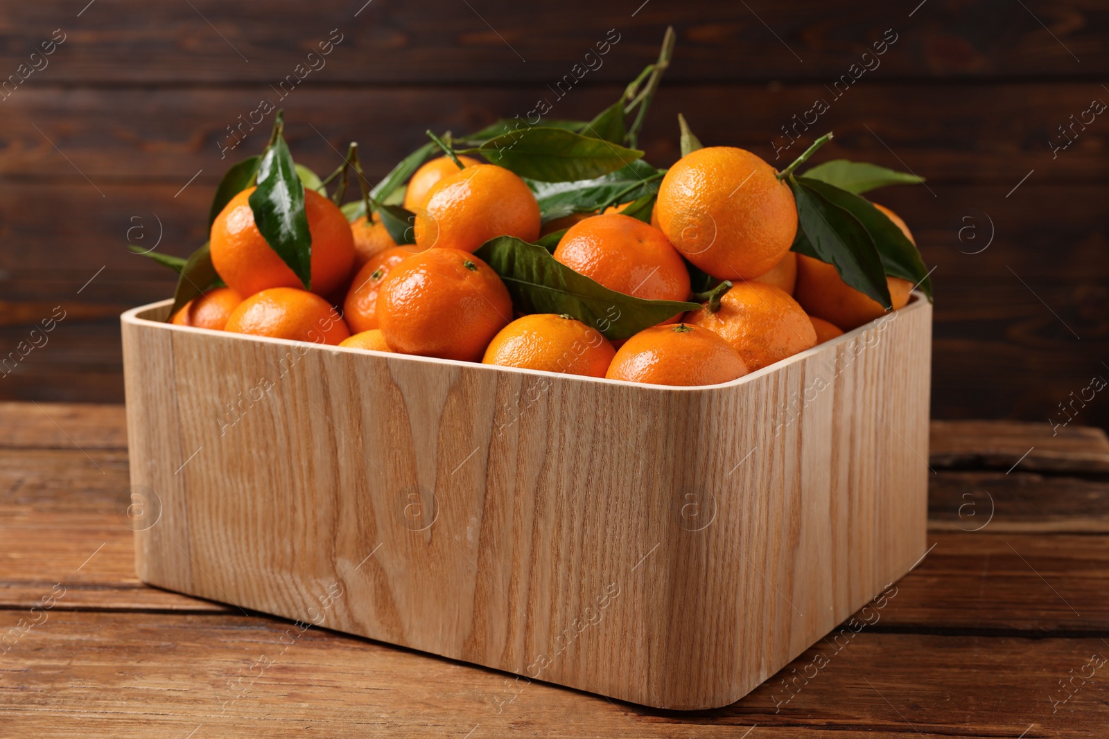 Photo of Fresh tangerines with green leaves in crate on wooden table