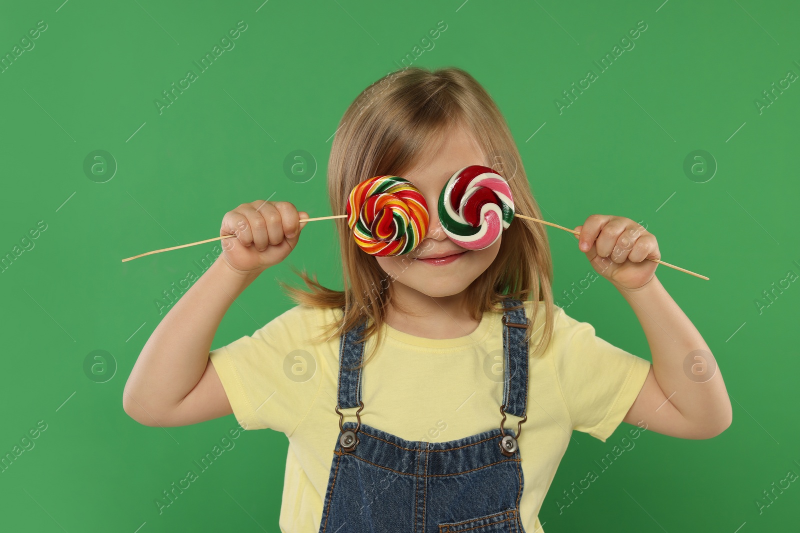Photo of Cute girl covering eyes with lollipops on green background