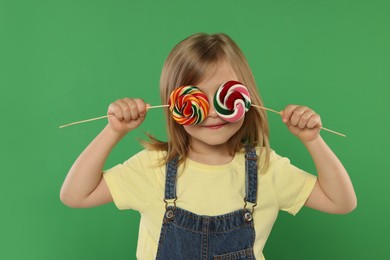 Cute girl covering eyes with lollipops on green background