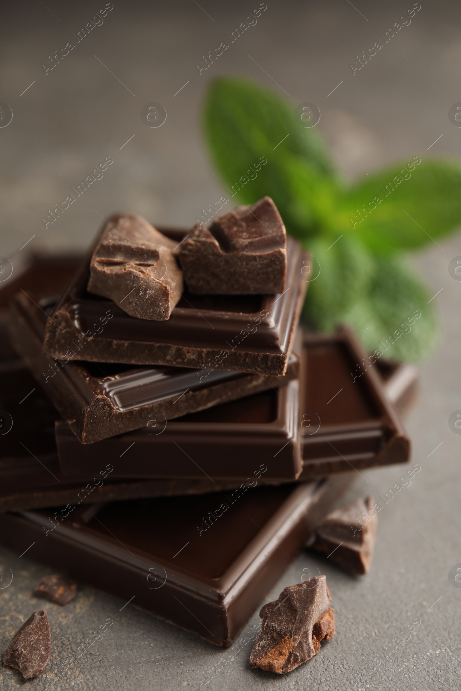 Photo of Tasty dark chocolate pieces with mint on grey table, closeup