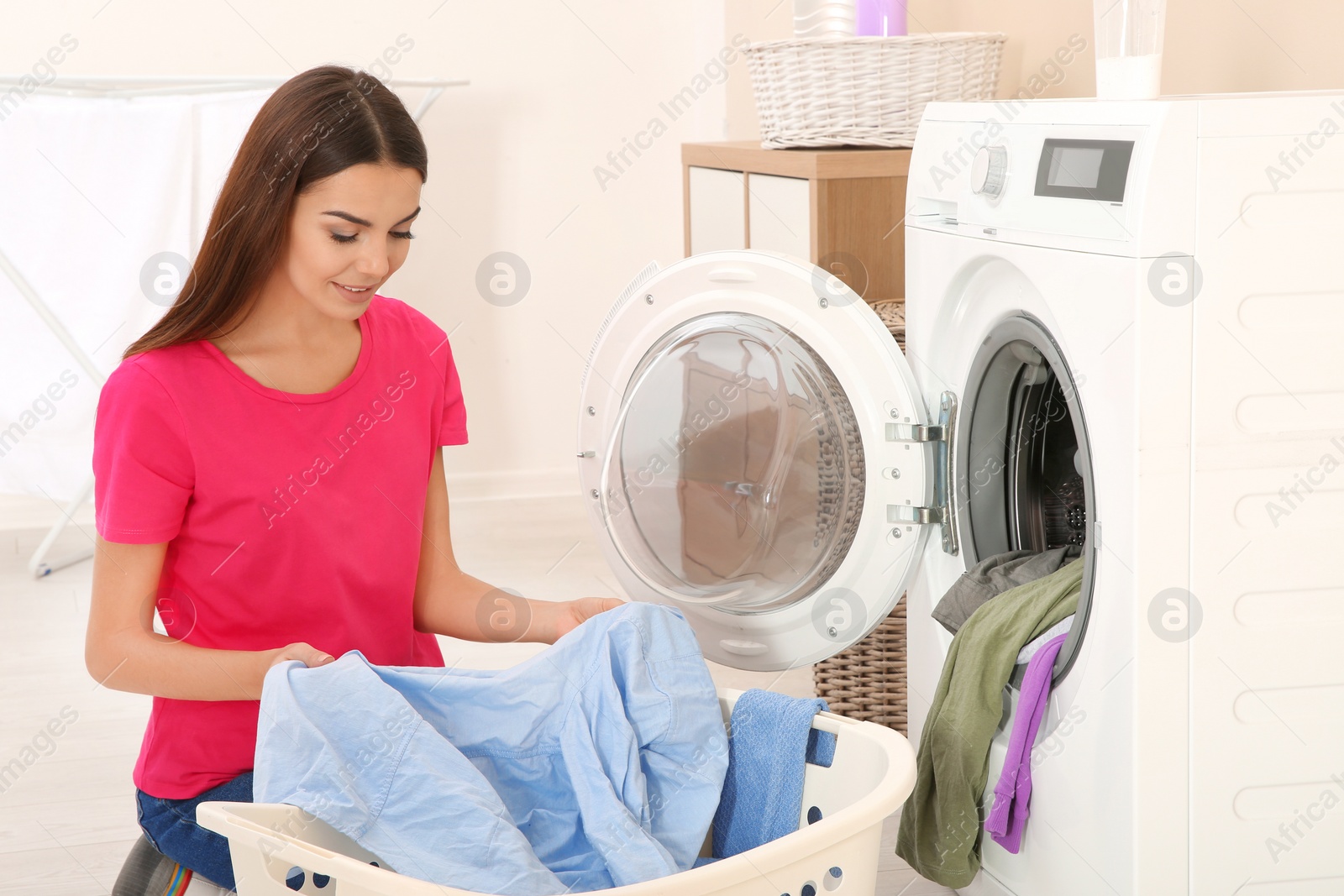 Photo of Young woman taking laundry out of washing machine at home